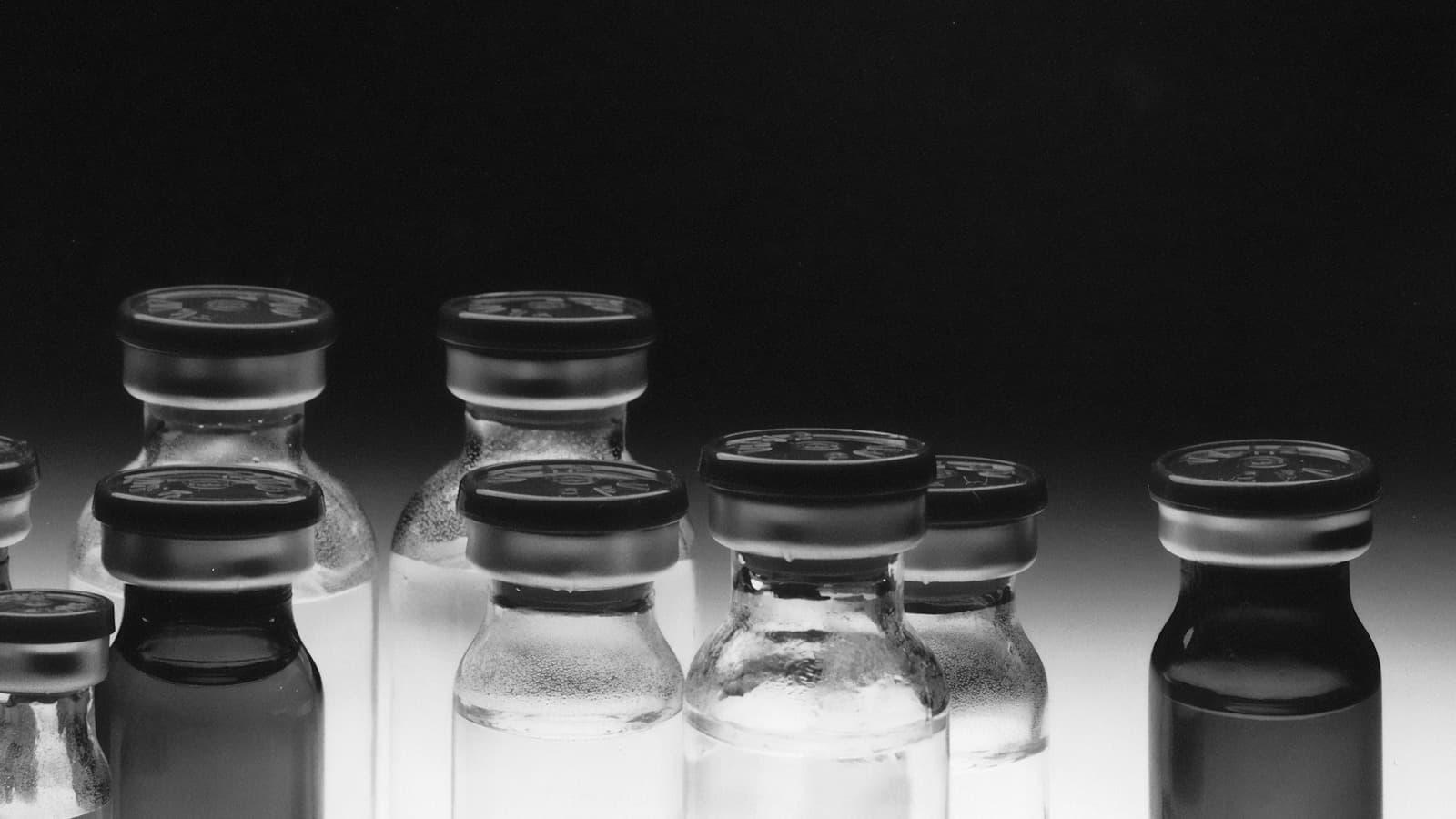 Stoppered glass medication vials standing in rows against a dark ground