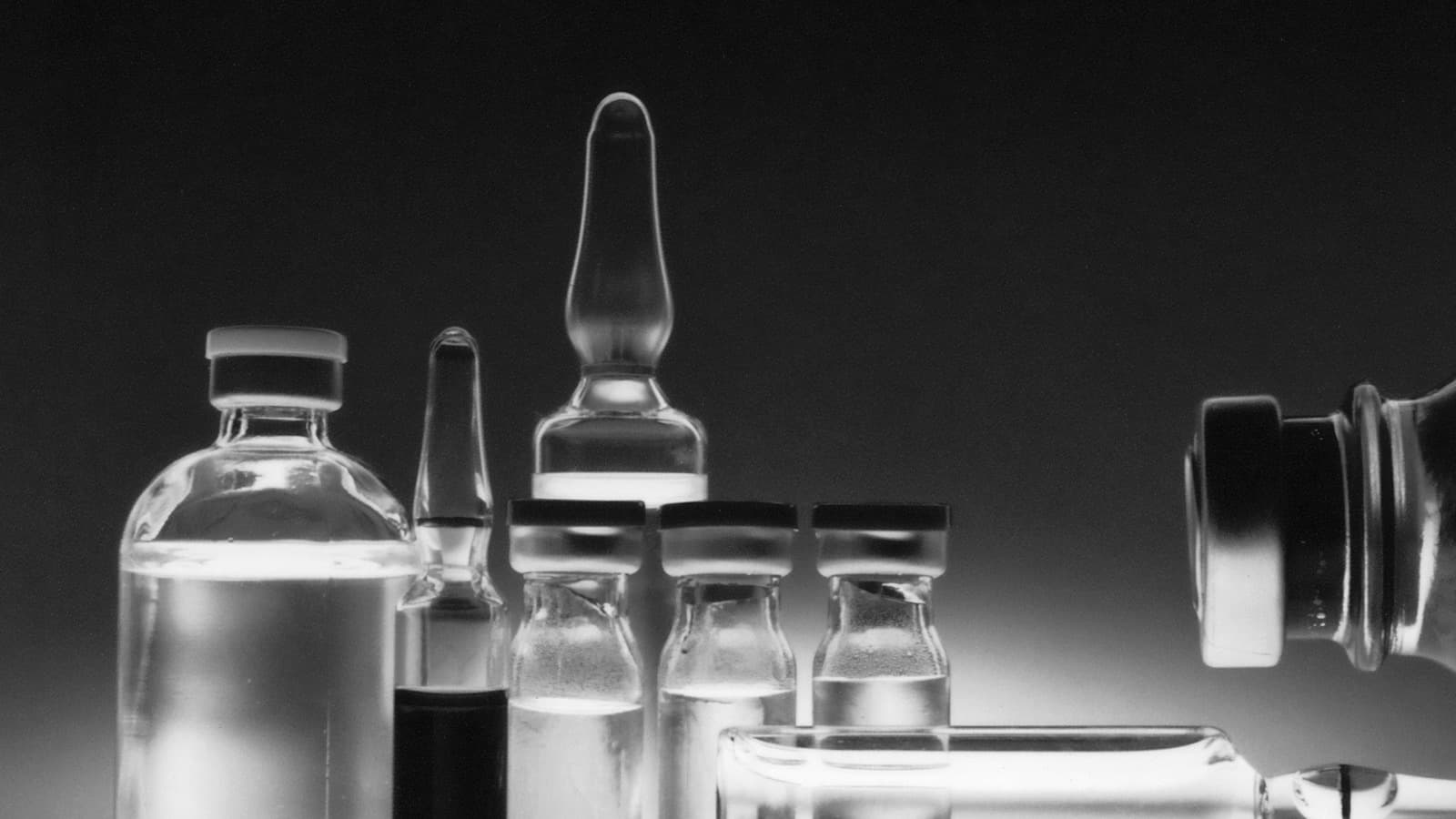 A close view of glass ampoules and small medication vials lit against black