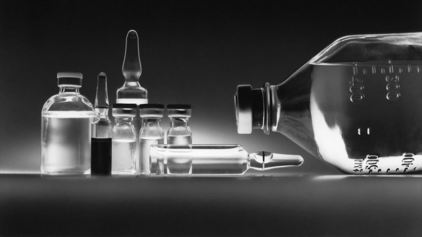 Glass medication vials, ampoules and an infusion bottle on a dark surface